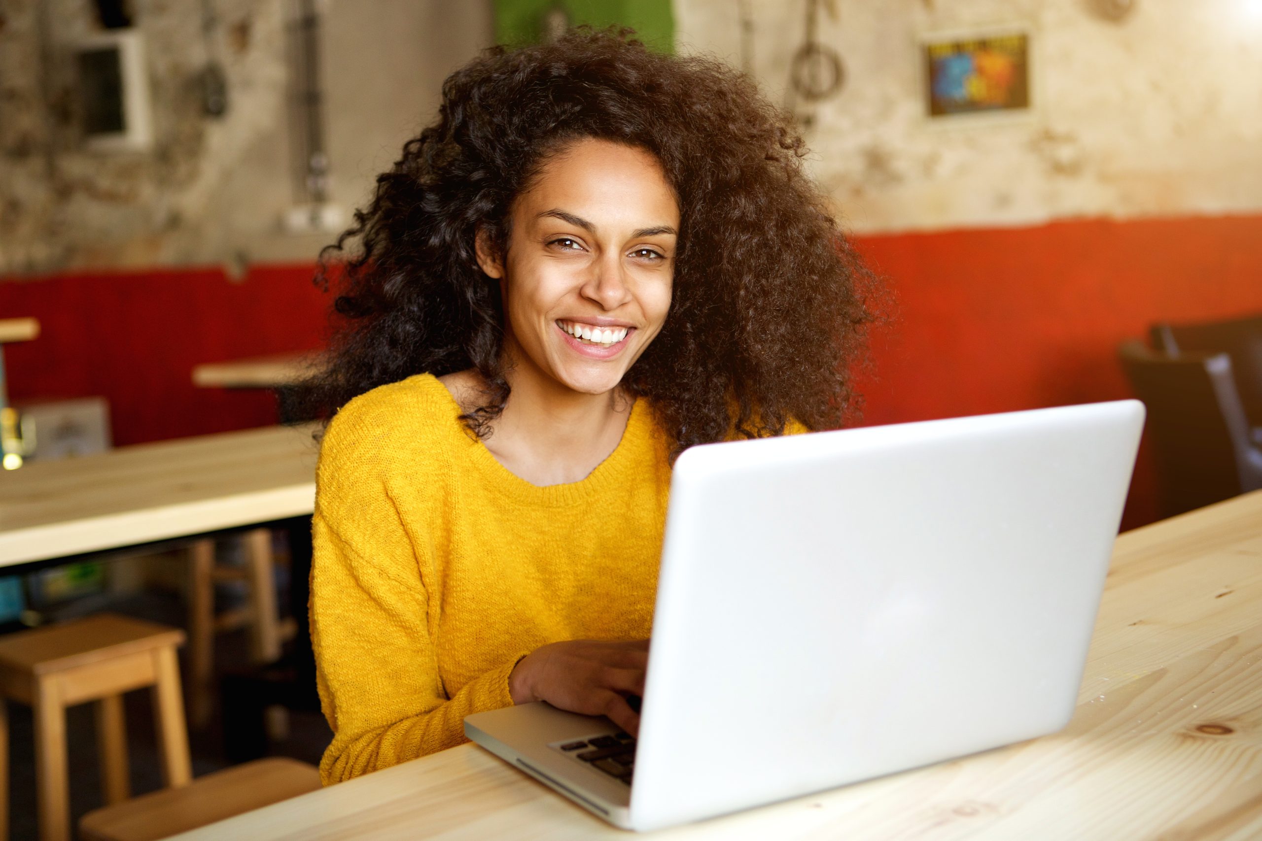 Portrait of smiling young african woman sitting in a cafe with laptop